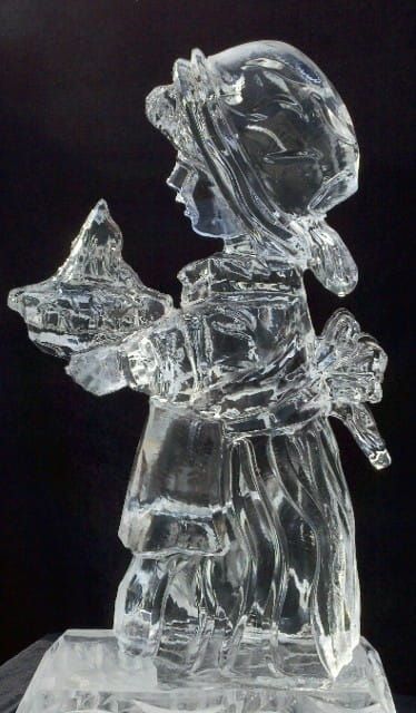 Clear glass figurine of a child holding a star, standing on a dark background.