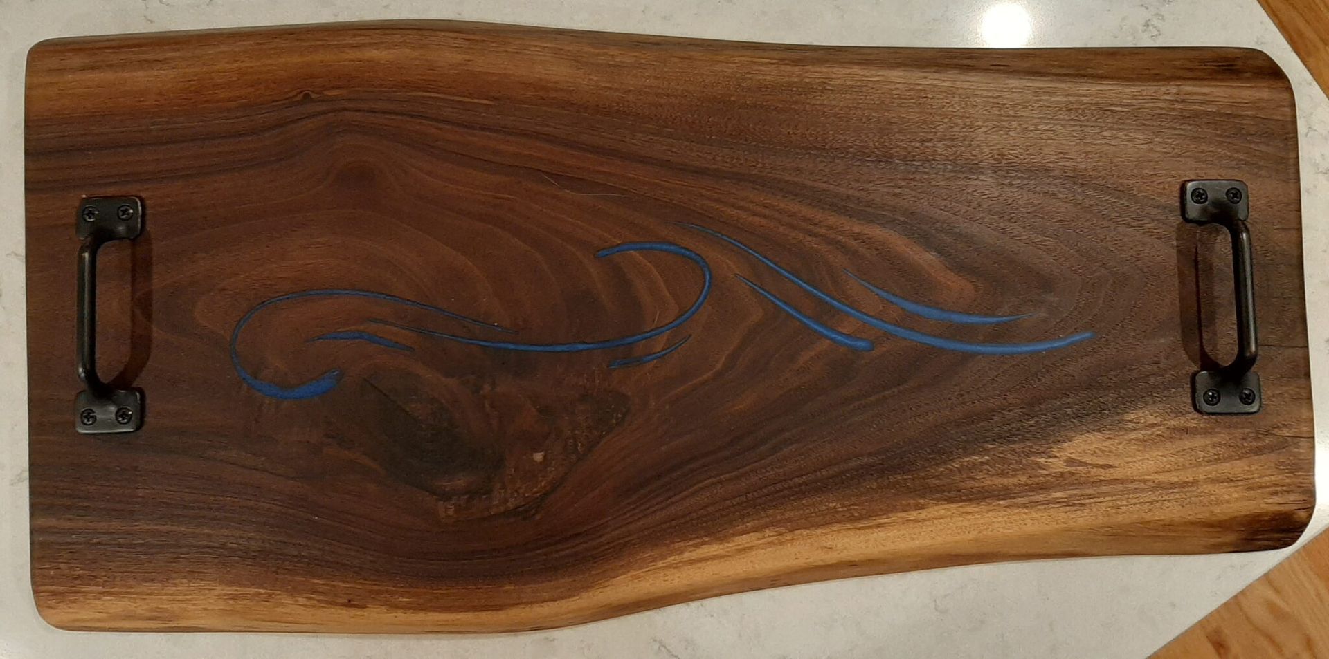 Wooden serving tray with black metal handles and blue wavy inlay design.