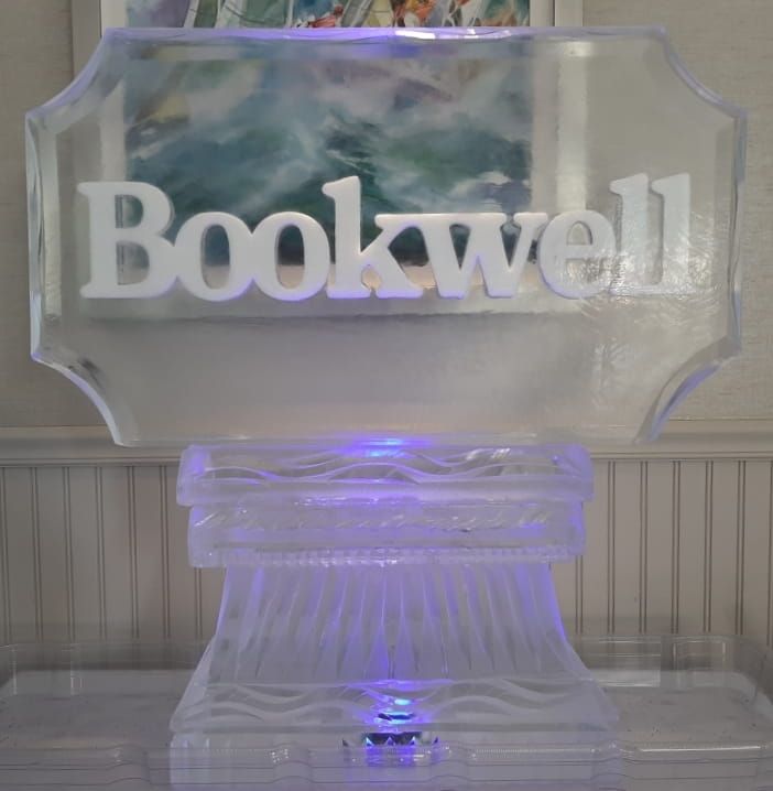 Translucent acrylic sign reading “Bookwell” lit with soft purple light against a striped wall.