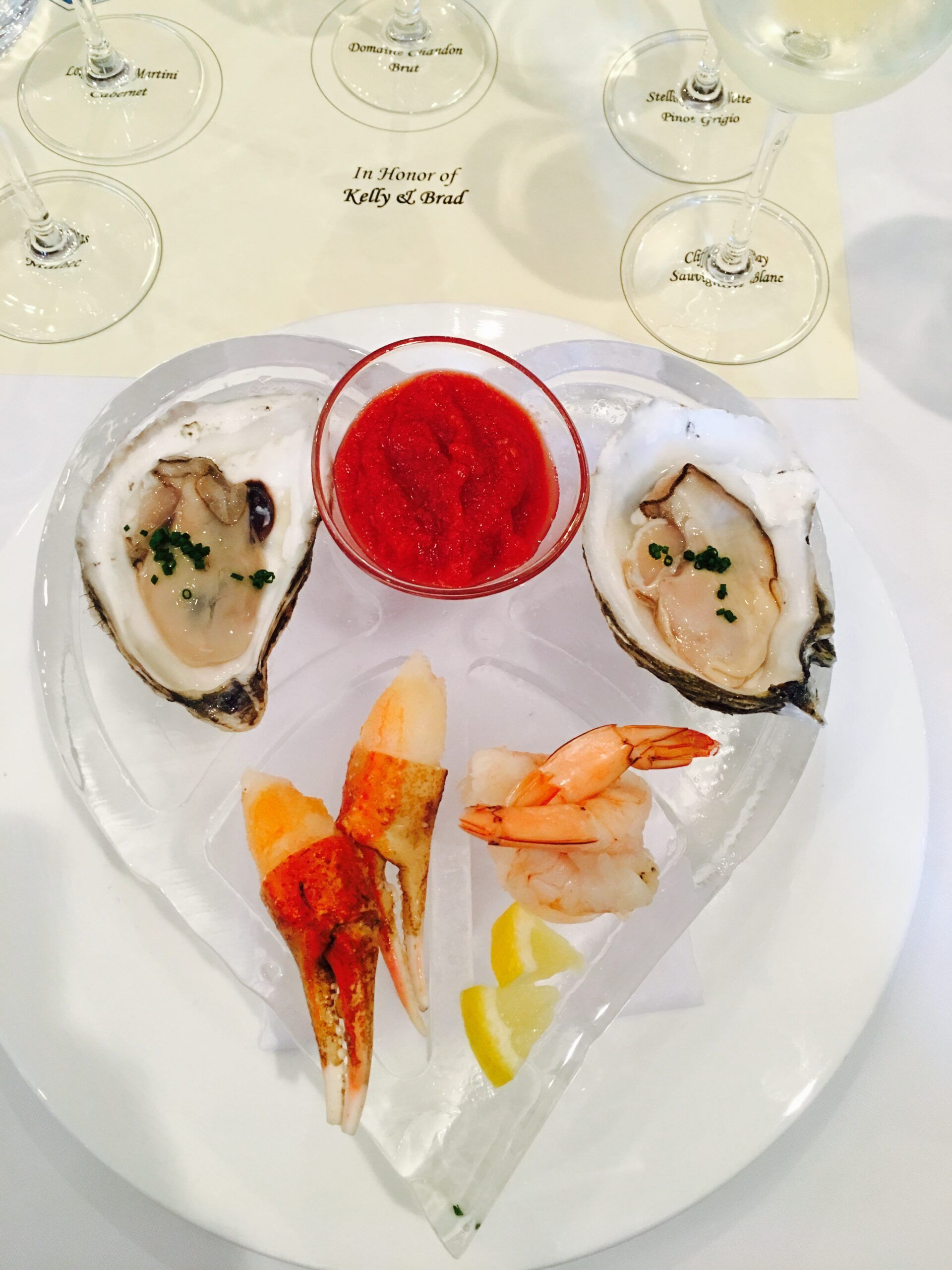 Seafood appetizer platter with oysters, red sauce, shrimp, and lemon wedges on a white plate