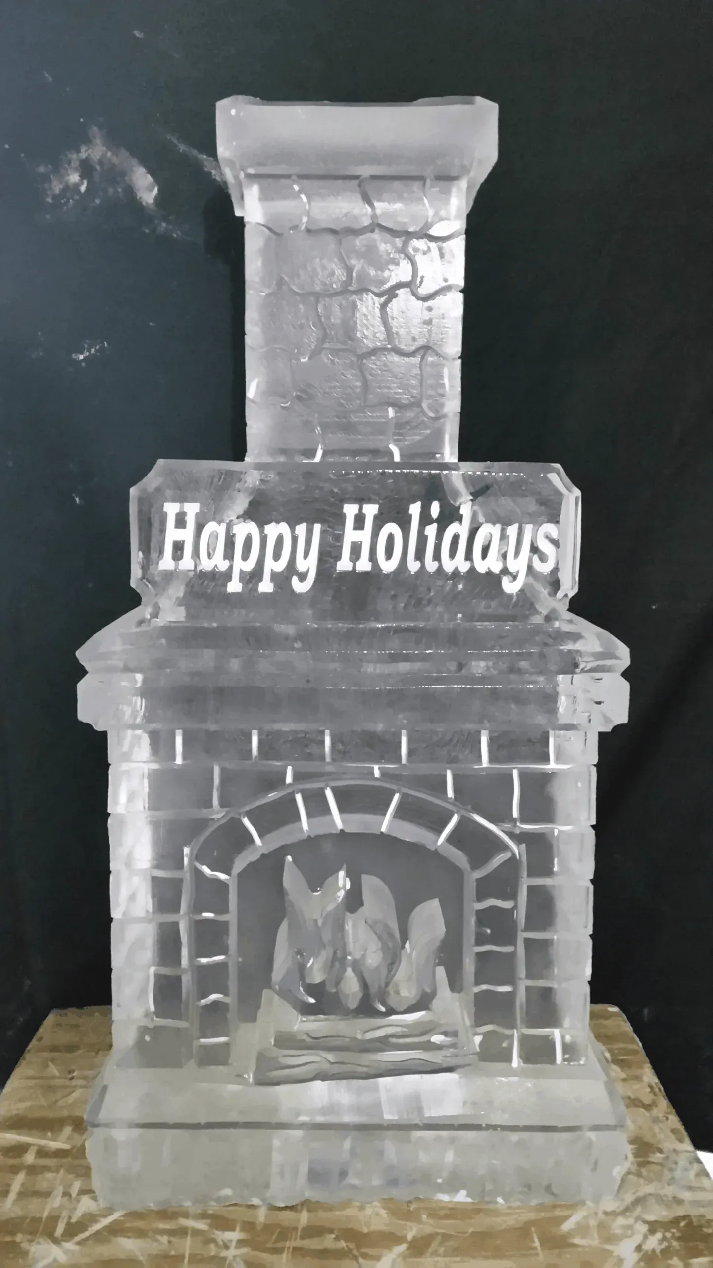 Silver fireplace decoration with “Happy Holidays” sign and small flames inside, against a dark background
