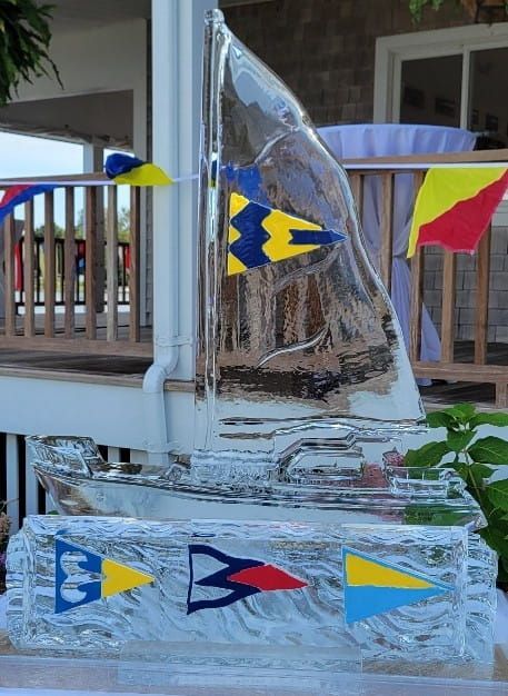 Glass sailboat sculpture with blue, yellow, and red flags on a porch railings backdrop
