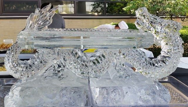 Clear ice sculpture of a bench or throne outdoors, with a building and windows in the background