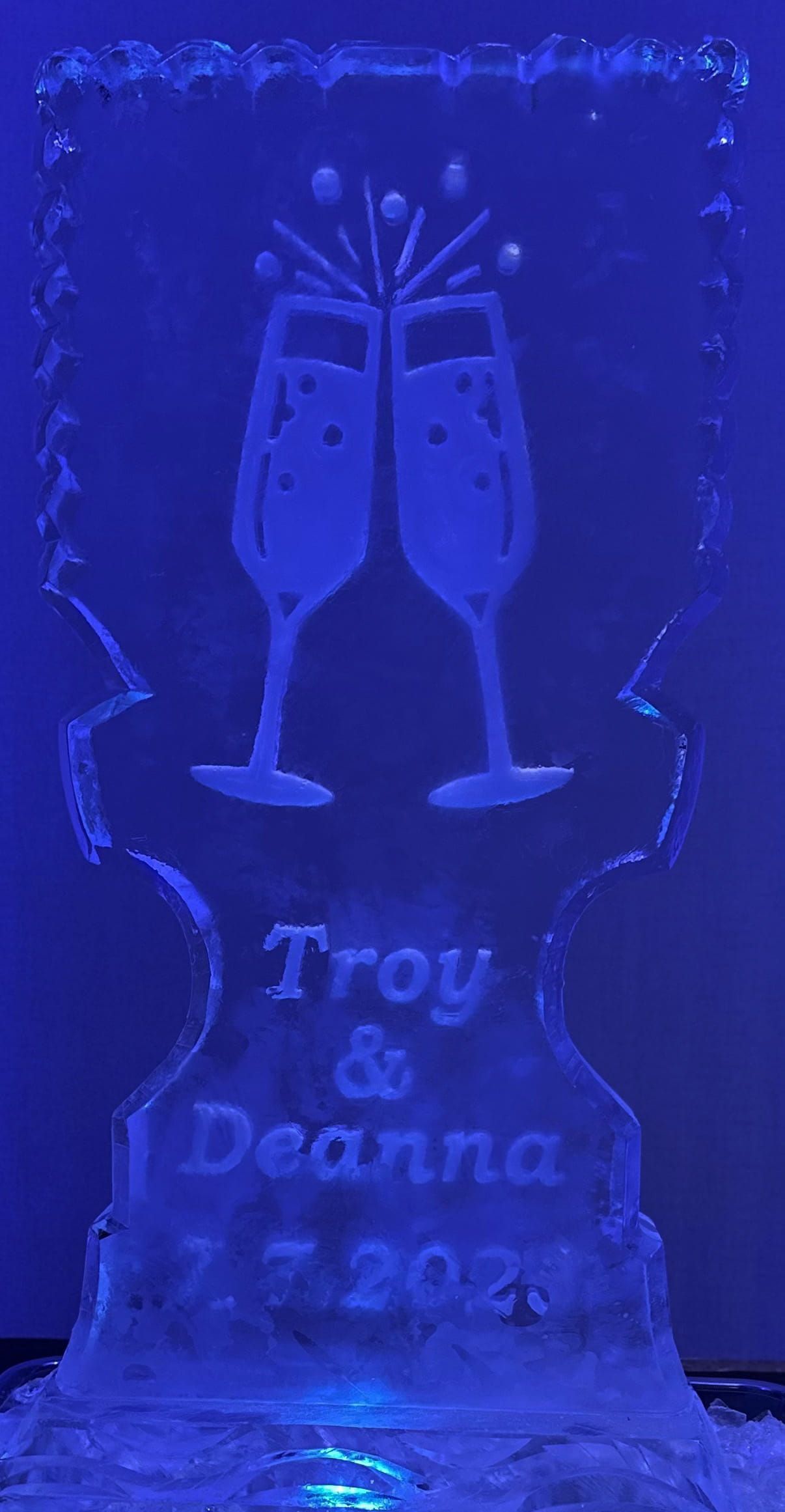 Blue-lit etched glass plaque with clinking champagne glasses and the name “Troy Deanna 7-2022”
