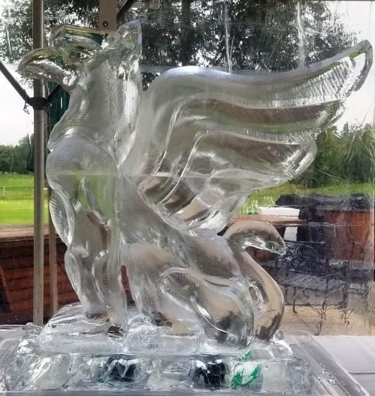Transparent glass unicorn sculpture with wings on a base, displayed indoors by a window