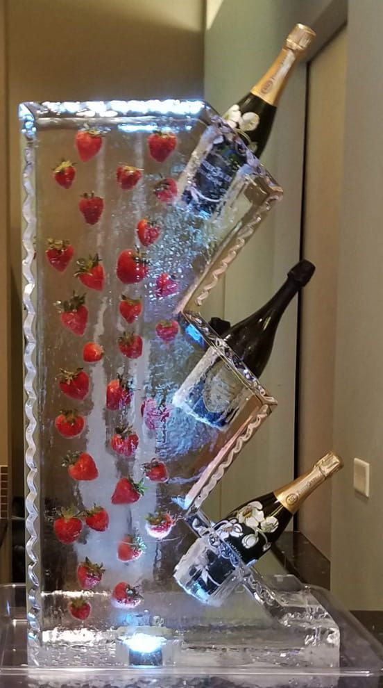 Decorative ice sculpture holding three tilted champagne bottles with red accents under blue lighting