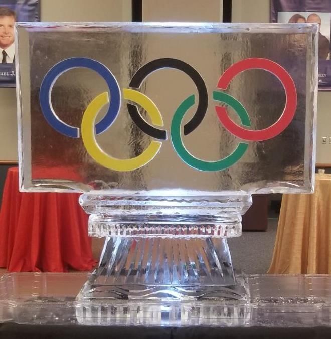 Clear plaque with Olympic rings logo on a pedestal, indoors.