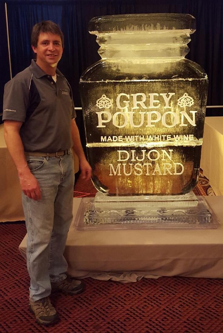 Man standing beside a Grey Poupon Dijon mustard ice sculpture at an event booth