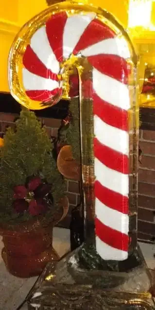 Candy cane-shaped glass ornament with red-and-white swirls on a holiday table display