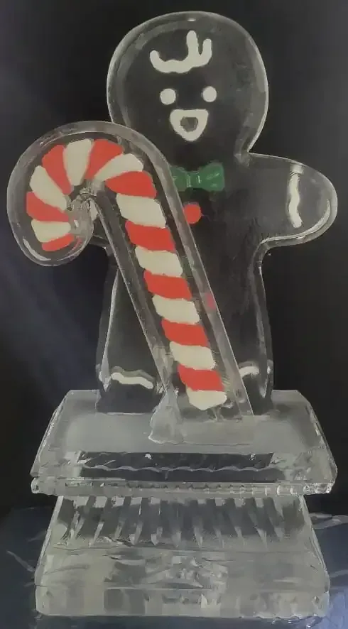 Black gingerbread figure with white icing holding a red-and-white candy cane on a clear stand.