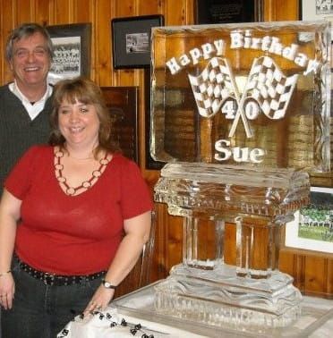 Woman and man beside a glass birthday ice sculpture reading “Happy Birthday 40 Sue”