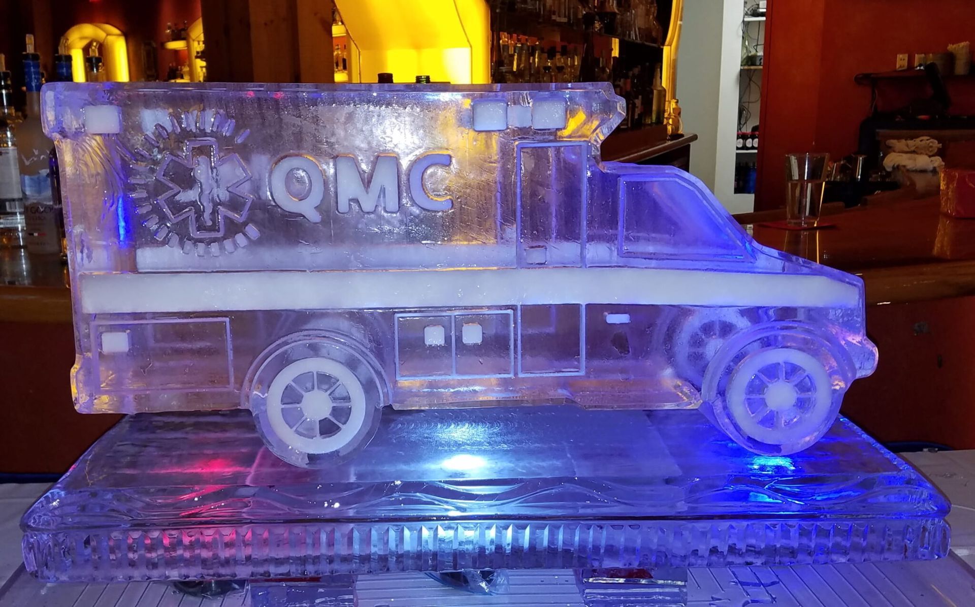 Clear acrylic truck model lit blue on a display stand, with “QMC” on the side.
