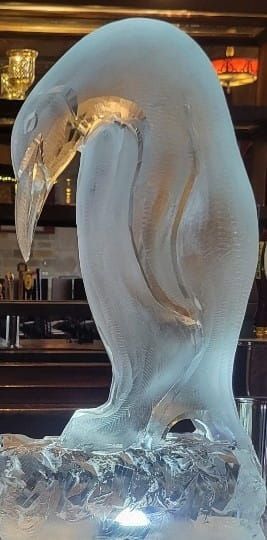 Transparent glass swan sculpture glowing on an ice base in a dimly lit interior.