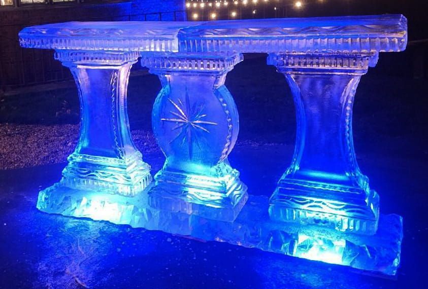 Blue-lit carved glass table or bench illuminated against a dark background