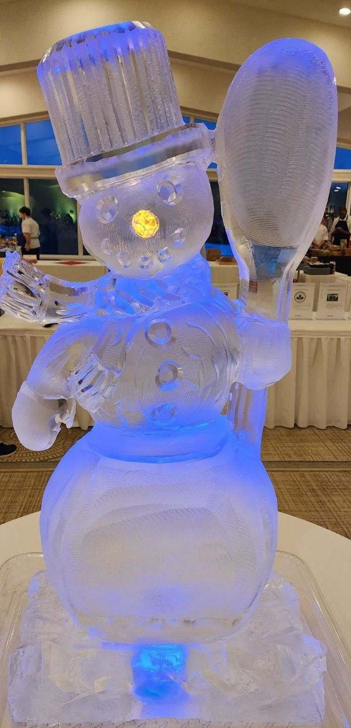 Blue-lit snowman ice sculpture wearing a hat and scarf on a pedestal indoors