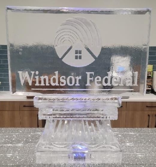 Clear acrylic Windsor Federal sign on a glass podium with a blue light, in a kitchen-like room.