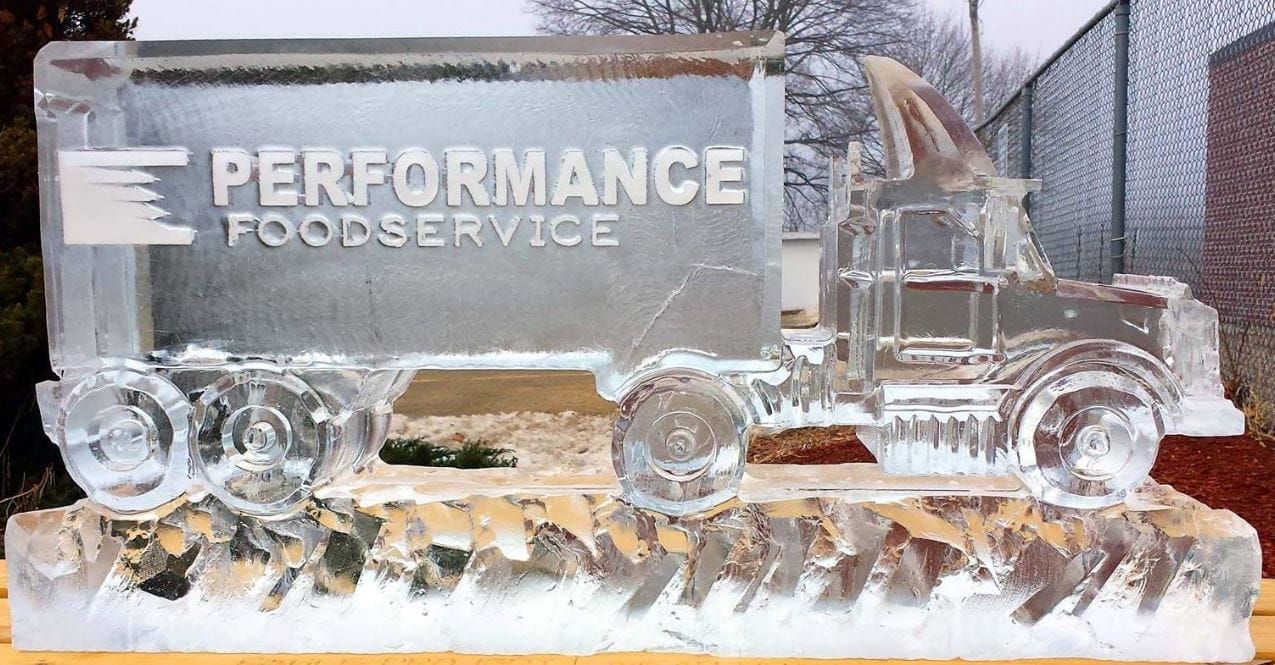 Ice sculpture of a foodservice truck and logo on a white base in a snowy outdoor setting