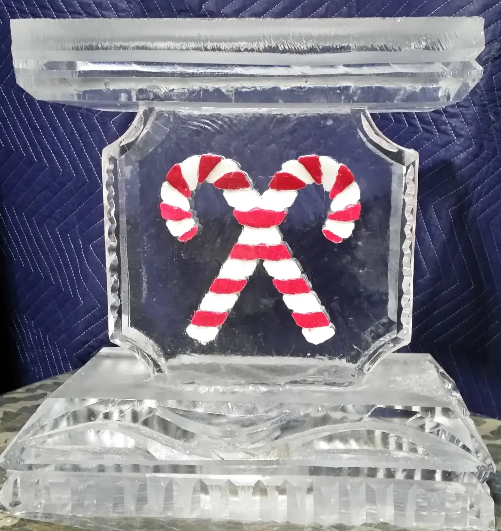 Red-and-white candy canes forming a crossed holiday symbol on a clear glass ornament against a dark blue background