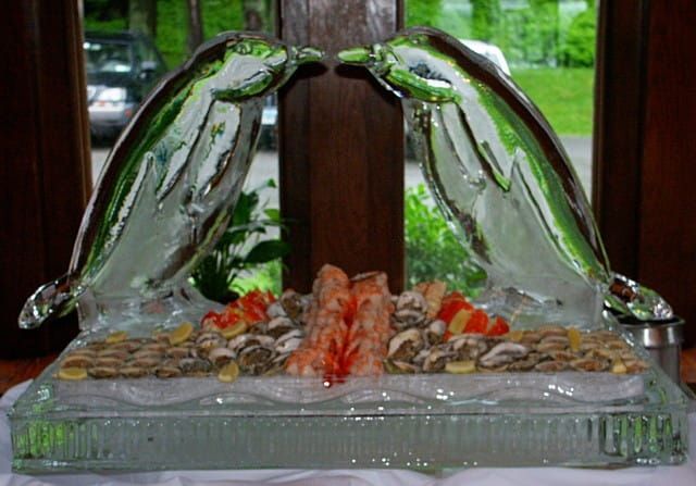 Glass fountain with two arched water streams over rocks and red accents on a tray indoors
