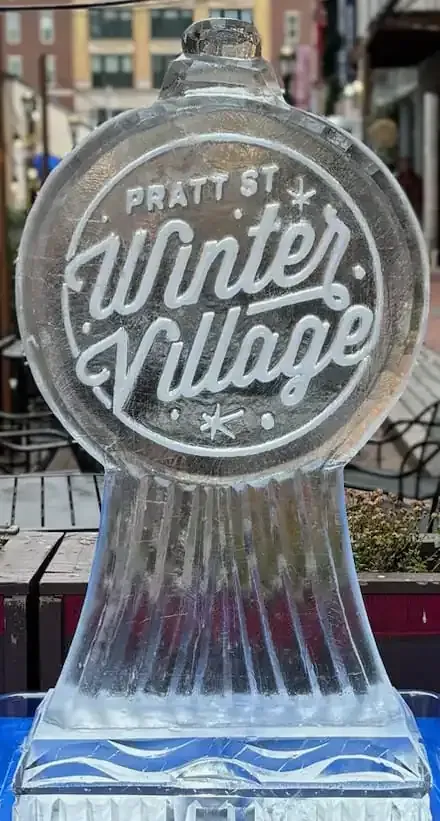 Pratt St Winter Village sign on an icy, frosted sculpture outdoors