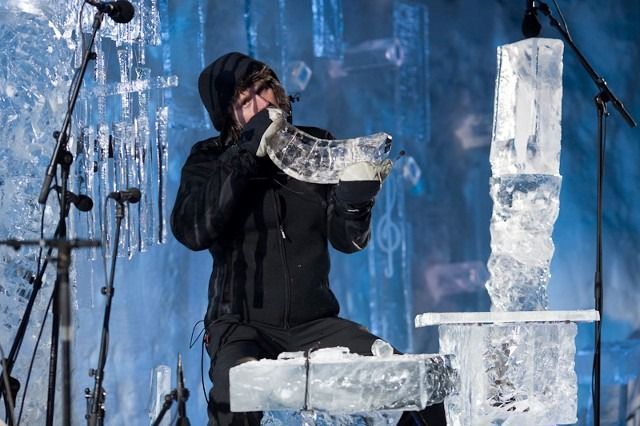 Person in black clothing holding a translucent ice sculpture on a blue stage