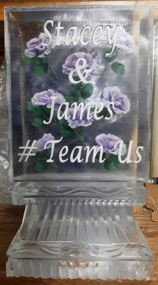 Clear glass award engraved “Stacey & James #TeamUs” with purple flowers inside.