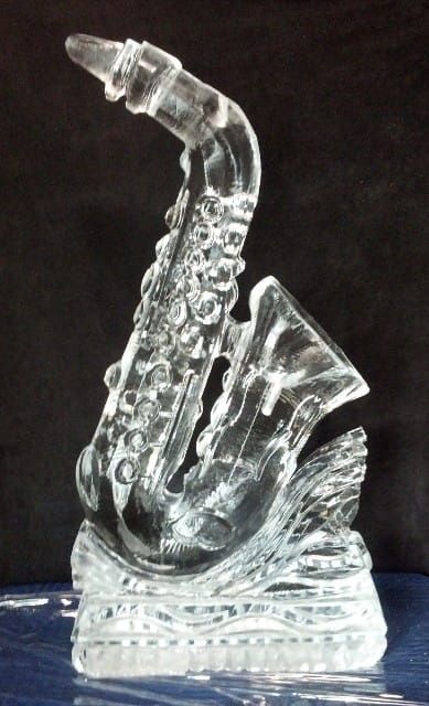 Clear glass saxophone figurine on a decorative base against a dark background