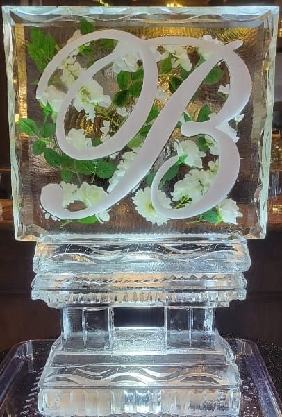 Clear glass monogram plaque with intertwined white letters on a reflective base