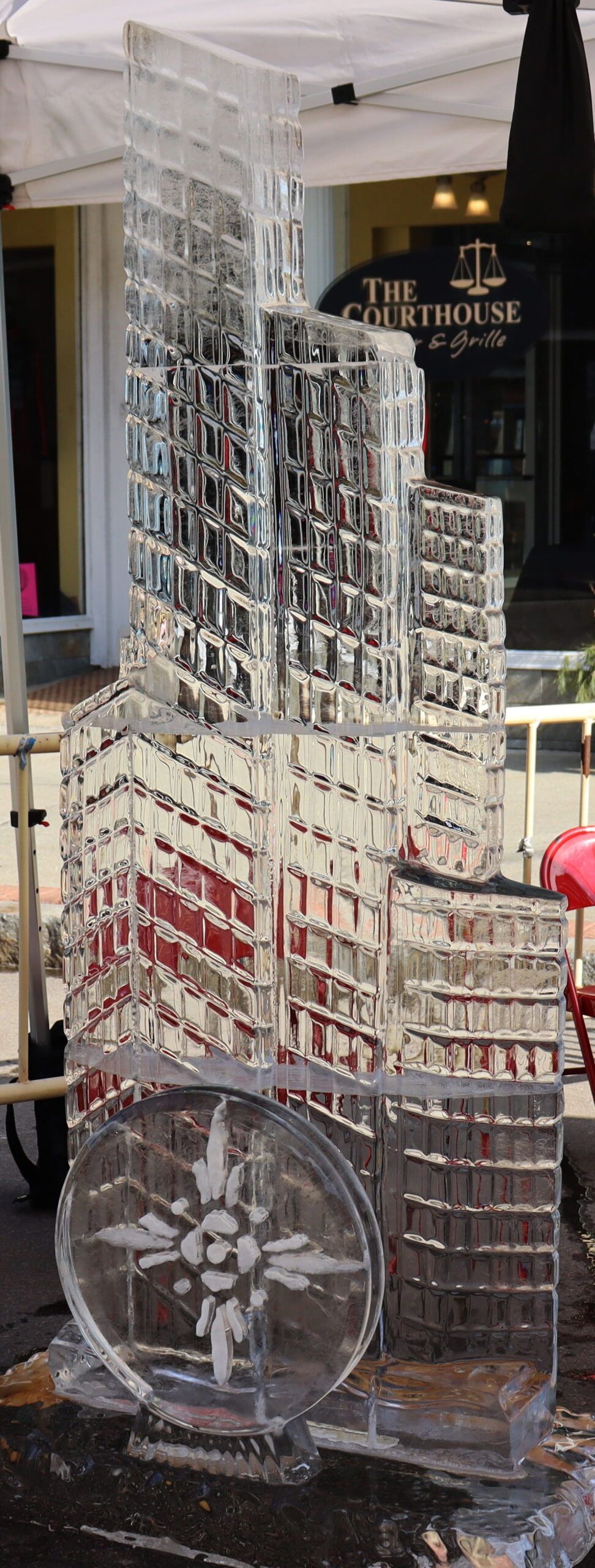 Clear glass skyscraper model with a round clock at the base, displayed indoors on a table.