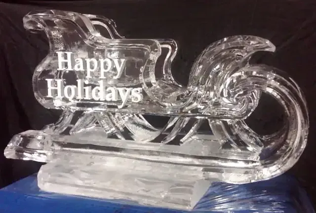 Clear glass holiday sleigh with “Happy Holidays” text on a blue surface.