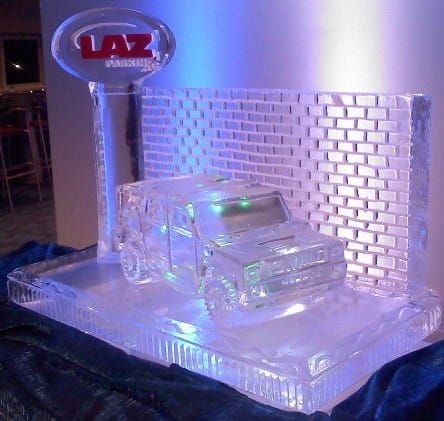 Clear acrylic model car on a mirrored base with a LAZ sign and brick-pattern backdrop, lit in purple-blue light