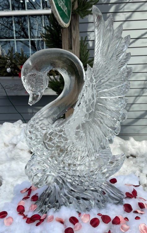 Clear glass swan sculpture on snow with red petals scattered around it