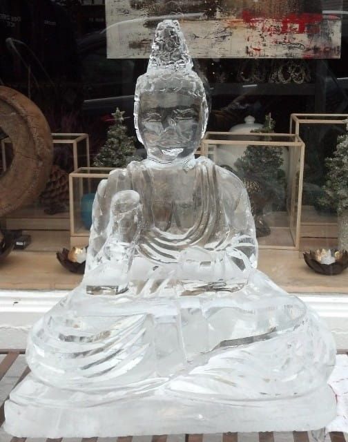 Transparent ice sculpture of a seated Buddha displayed in a storefront window