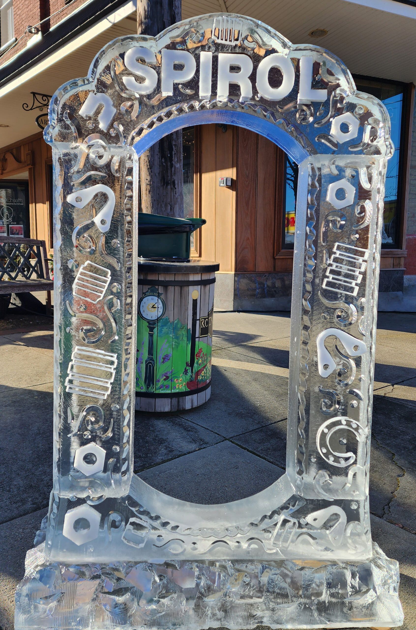 Decorative stone Spirol sign with an arch opening, set outdoors on a sunlit street.