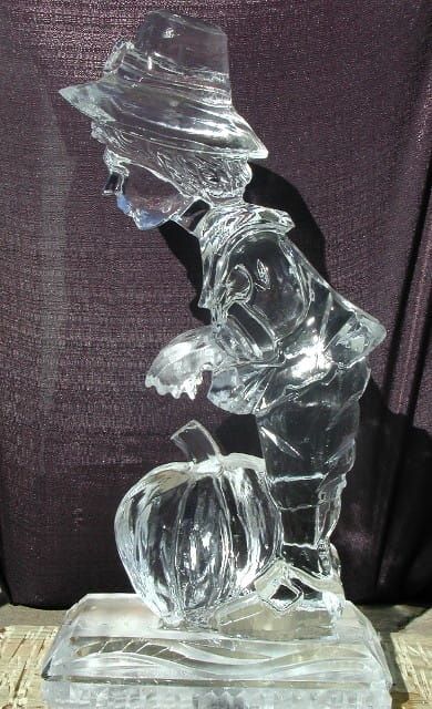 Clear glass figurine of a hatted person leaning over a basket on a rectangular base