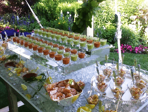 Outdoor buffet table with rows of small dessert cups, fruit bowls, and appetizers in a garden setting