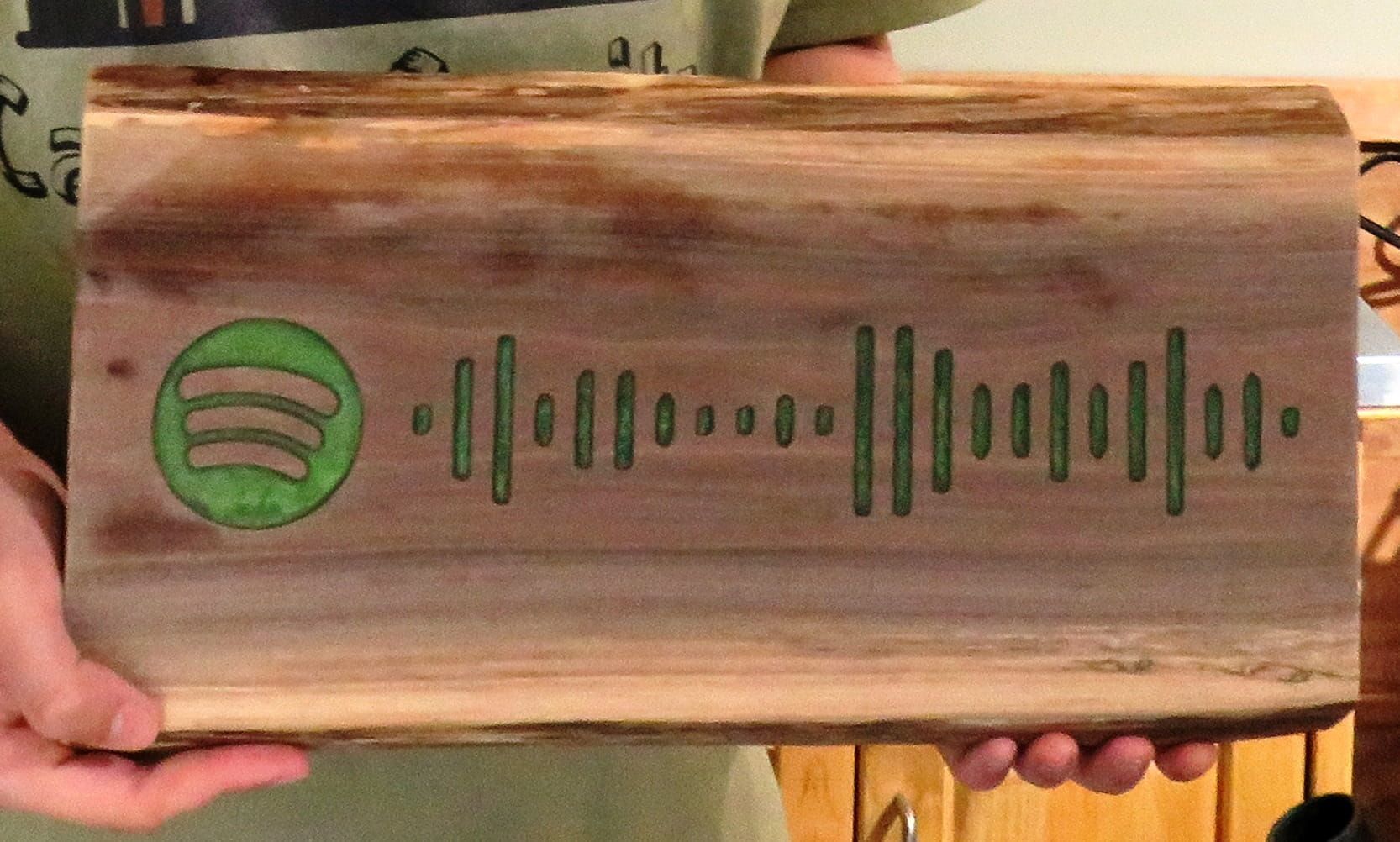 Wooden plaque with green Spotify logo and code, held by hands