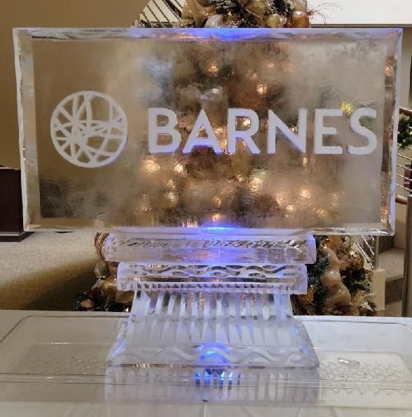 BARNES logo on a clear plaque with a decorative white stand, lit in a festive indoor setting