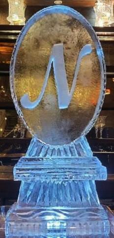 Blue crystal award with a stylized silver N on a clear pedestal, indoors under warm lights