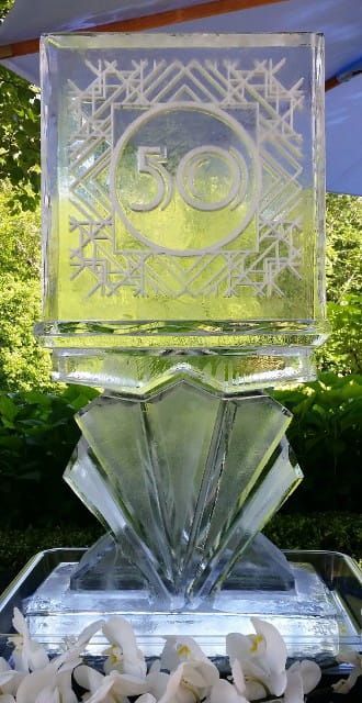Clear glass trophy with a circular “50” emblem and white flowers at the base outdoors