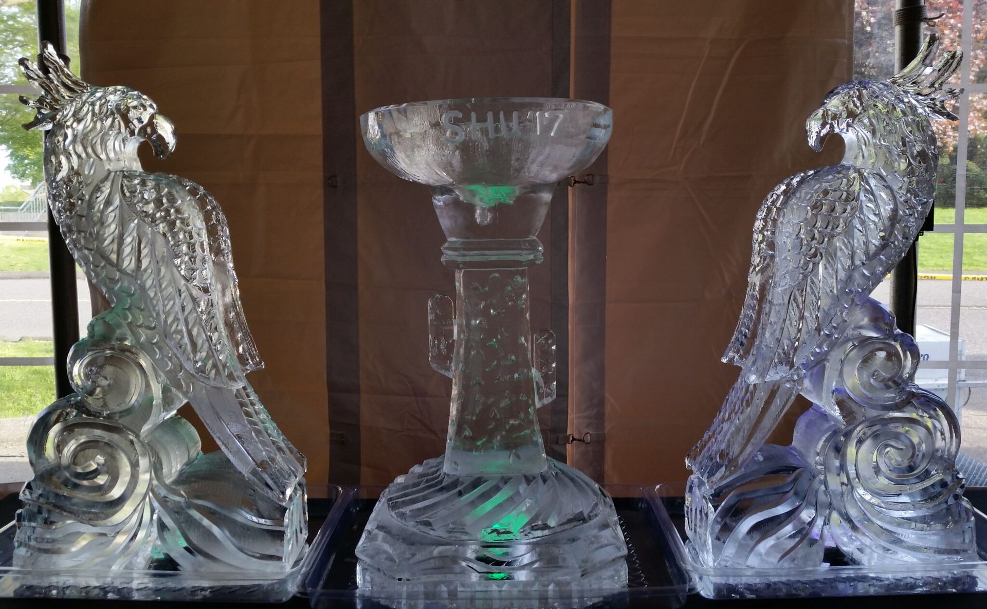 Two ornate clear-glass bird sculptures flanking a tall glass vase on a dark display shelf