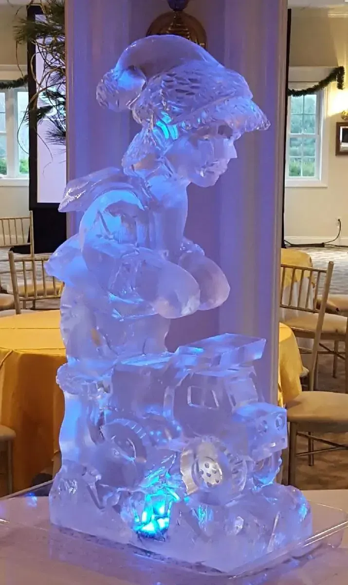 Blue-lit ice sculpture of a boy playing an accordion, displayed indoors on a pedestal.