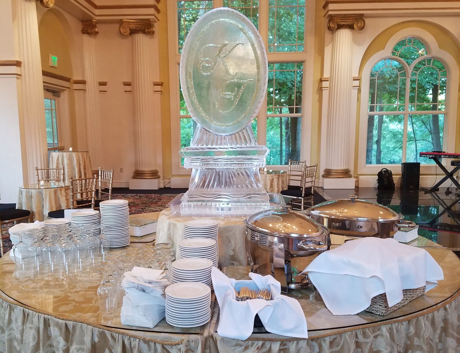 Elegant buffet table with glassware, plates, and covered dishes in a bright room with arched windows.