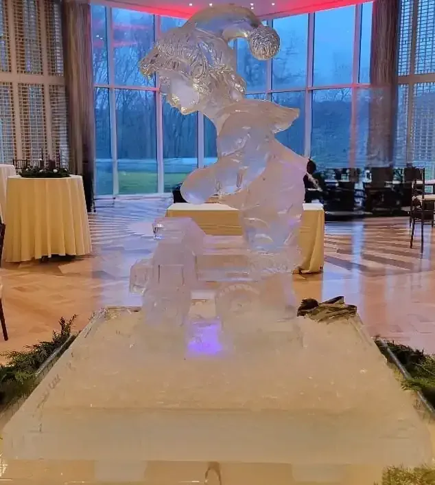 Ice sculpture centerpiece in a grand ballroom with large windows and warm lighting.