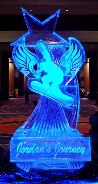Blue illuminated ice sculpture of a leaping dancer with wings and star, reading “Jordan’s Journey” at the base