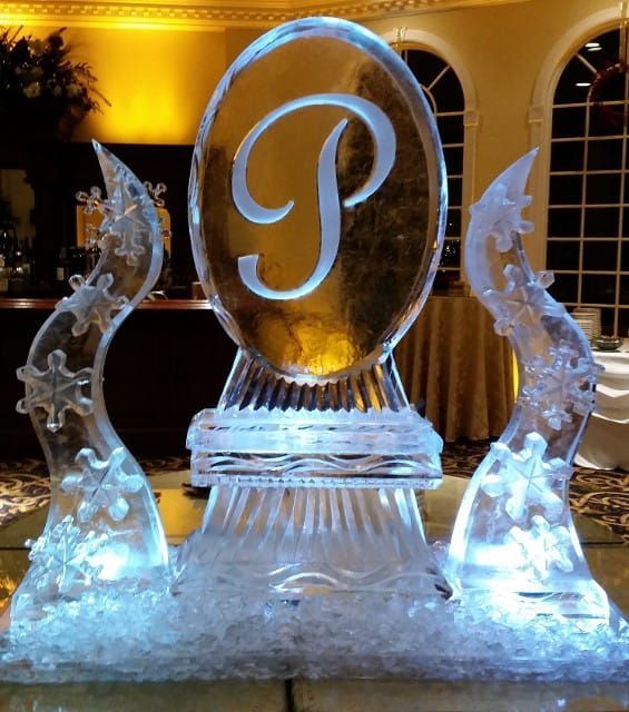 Ice sculpture with a monogram “P” at a formal event, lit in warm gold and blue.