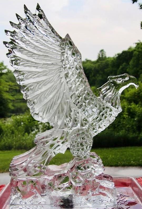 Clear glass eagle sculpture with raised wings on a red table outdoors