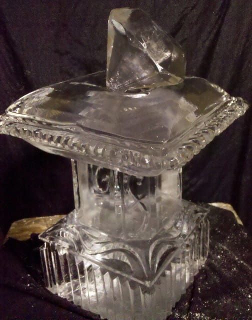 Clear glass decorative box with etched sides and a faceted crystal on top against a dark background