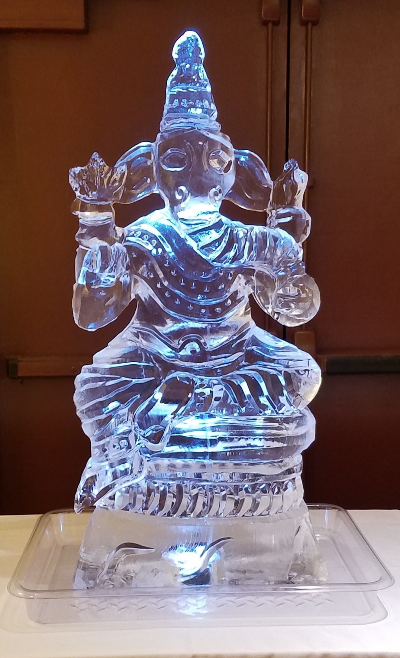 Blue-lit translucent statue on a clear base, set against a brown background.