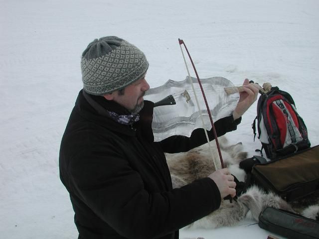 Person in black jacket and gray knit hat studying a map on snowy ground beside backpack and gear
